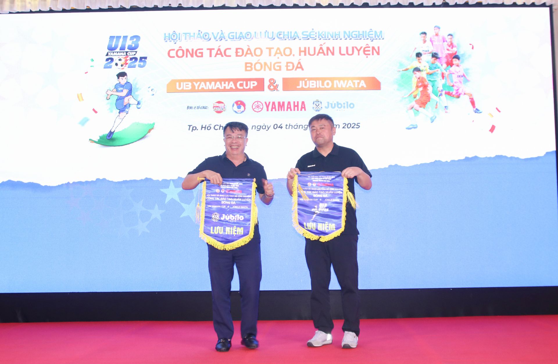 Nguyễn Phan Khuê – Tổng Biên tập Báo Thiếu niên Tiền phong & Nhi Đồng và ông Shinozaki Hideaki – đại diện học viện Jubilo Iwata (Nhật Bản) trao tặng cờ kỷ niệm, ghi dấu hoạt động giao lưu huấn luyện bóng đá trẻ Việt Nam – Nhật Bản - Ảnh: Nguyễn Thắm.
