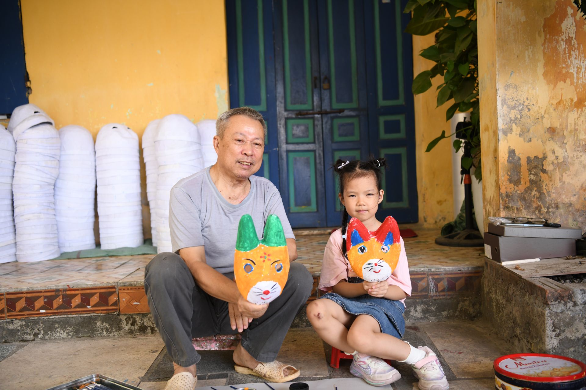 Bác Đông và một bạn nhỏ khoe thành quả: những chiếc mặt nạ mèo ngộ nghĩnh, đầy màu sắc Trung thu.