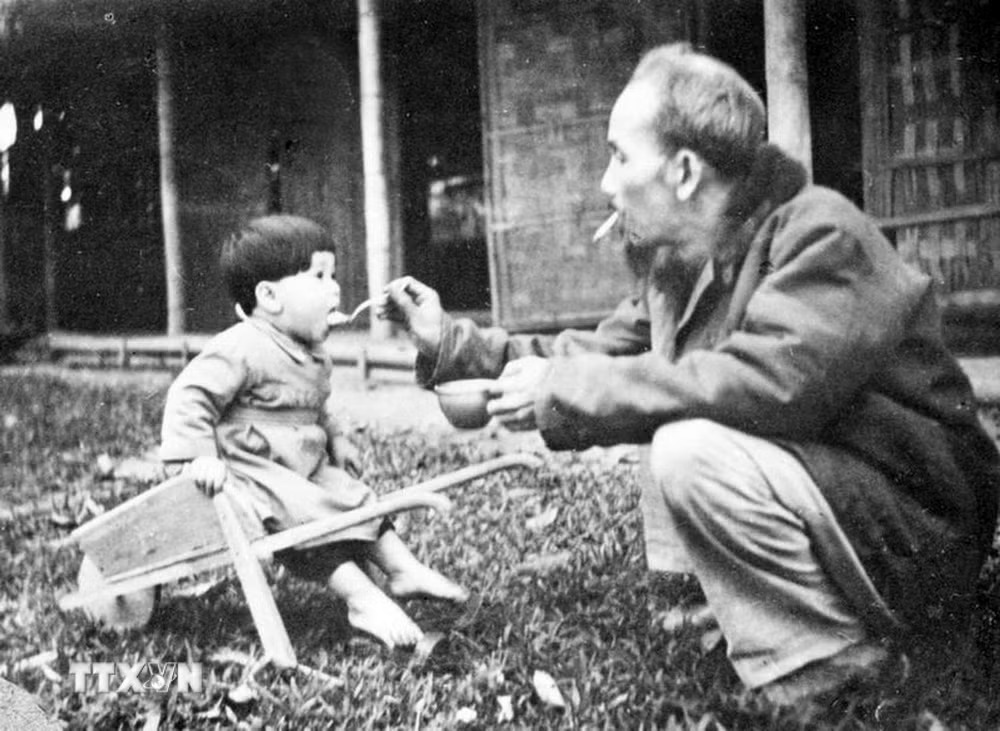 B&aacute;c Hồ b&oacute;n cơm cho một ch&aacute;u b&eacute; khi đến thăm trại nhi đồng ở chiến khu Việt Bắc (1950). Ảnh: Tư liệu TTXVN.